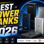 A graphic titled "BEST POWER BANKS IN 2026" featuring a bold yellow-and-white headline on the left and a collection of modern power banks from Ambrane, URBN, boAt, Xiaomi (Mi), and Duracell displayed on the right against a futuristic blue and black background. Icons at the bottom highlight ultra-fast charging, premium safety, high battery capacity, and travel-friendly design